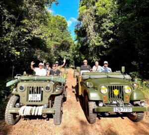 Kolona historických džípů americké armády projíždí tropickou krajinou.