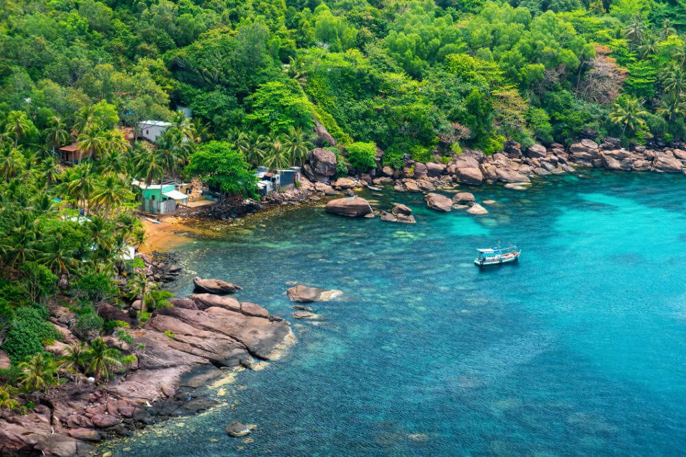 Tropické pobřeží Phu Quocu s tyrkysovou vodou, loďkou a džunglí sahající až k moři