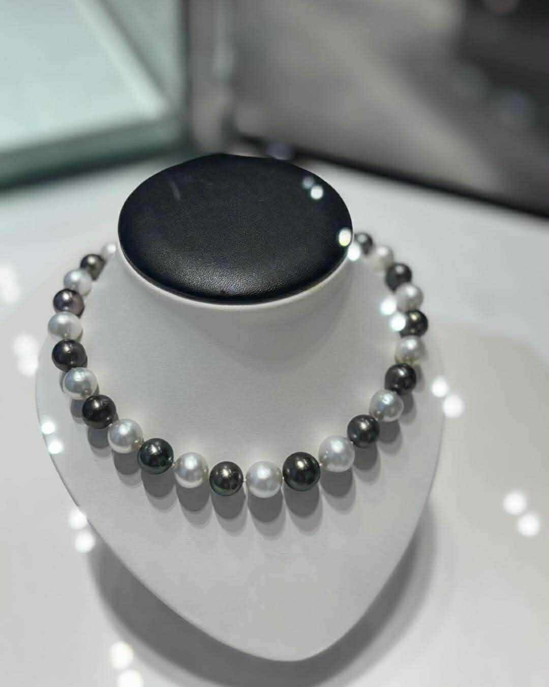 Luxusní náhrdelník z bílých a černých perel na výstavním stojanu
