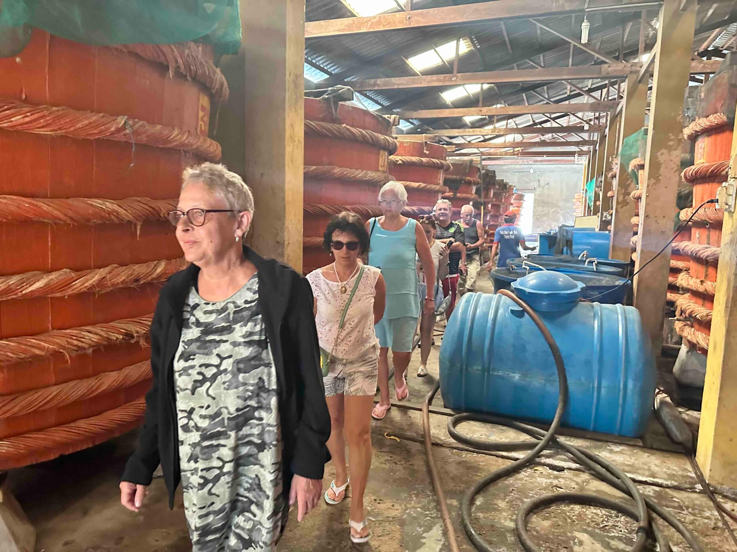 Skupina turistů prochází mezi obřími sudy v továrně na rybí omáčku